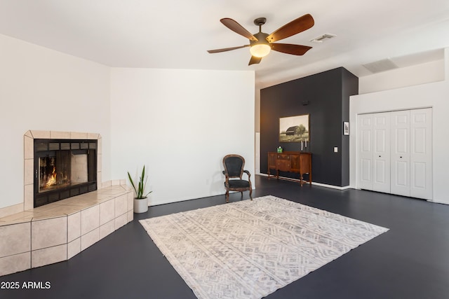interior space featuring finished concrete floors, a tiled fireplace, a ceiling fan, and visible vents