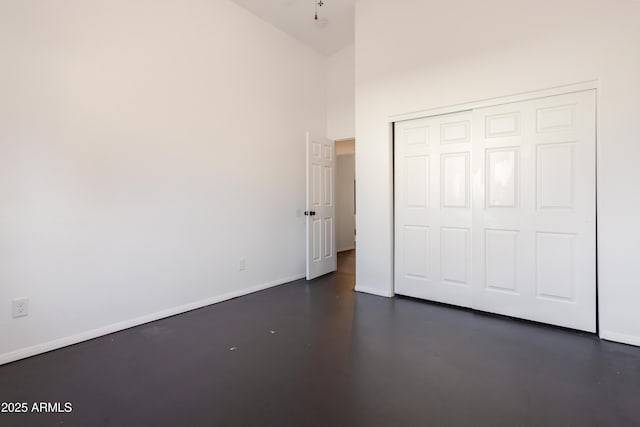 unfurnished bedroom featuring high vaulted ceiling, baseboards, concrete flooring, and a closet