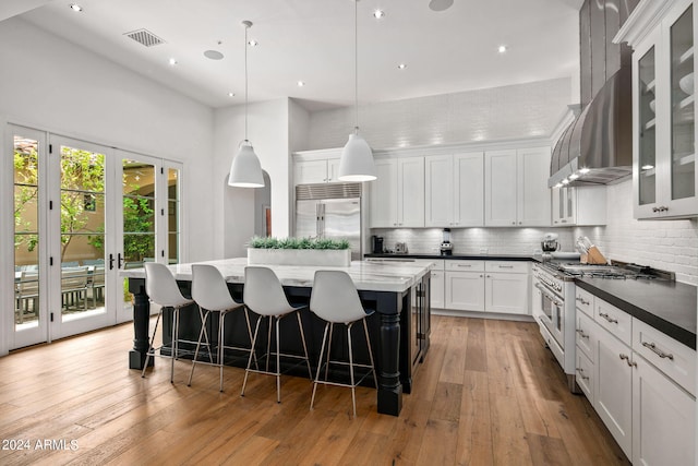 kitchen with white cabinets, premium appliances, a large island, glass insert cabinets, and decorative light fixtures