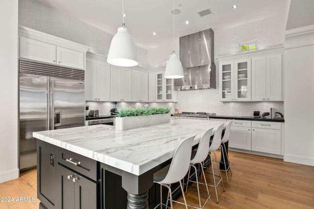 kitchen featuring white cabinets, wall chimney exhaust hood, a large island, glass insert cabinets, and stainless steel appliances