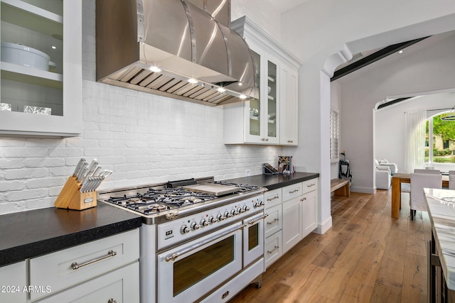 kitchen featuring white cabinetry, range hood, double oven range, dark countertops, and glass insert cabinets