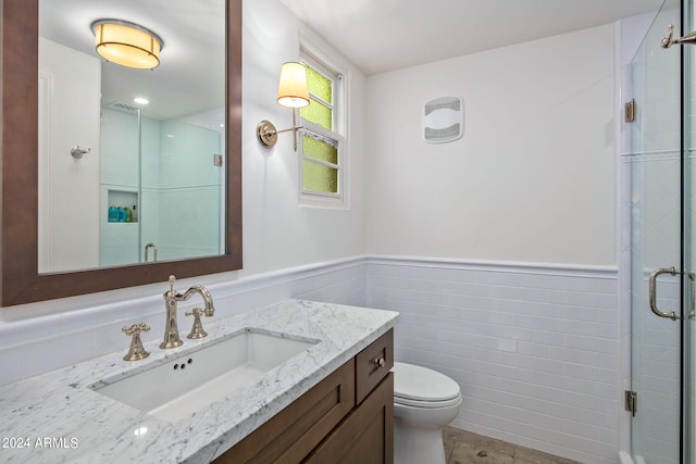 bathroom featuring a stall shower, wainscoting, toilet, vanity, and tile walls