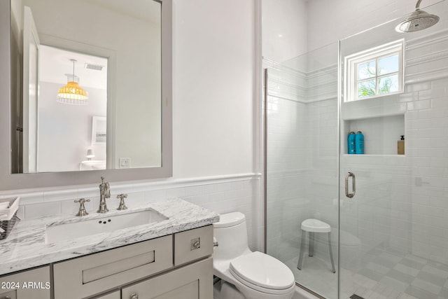 bathroom with toilet, vanity, tile walls, wainscoting, and a stall shower