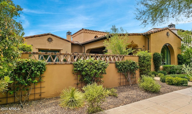 view of front of property with a garage, a chimney, a tiled roof, fence, and stucco siding