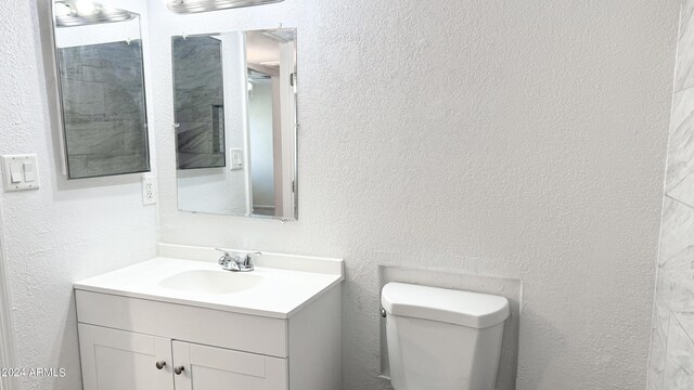 bathroom with toilet, a textured wall, and vanity