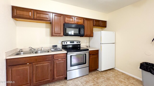 kitchen with black microwave, a sink, stainless steel range with electric cooktop, light countertops, and freestanding refrigerator