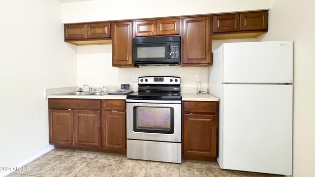 kitchen featuring black microwave, a sink, light countertops, freestanding refrigerator, and stainless steel electric stove