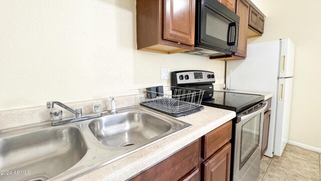 kitchen featuring electric range, brown cabinetry, light countertops, black microwave, and a sink