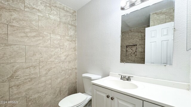 bathroom with a textured wall, vanity, and toilet