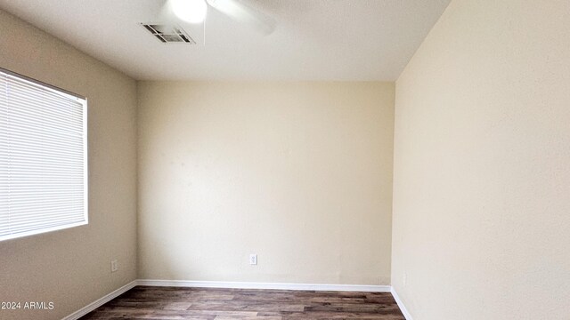 spare room featuring dark wood-style floors, ceiling fan, visible vents, and baseboards