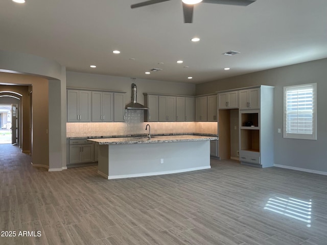 kitchen featuring visible vents, gray cabinetry, wall chimney range hood, decorative backsplash, and a kitchen island with sink