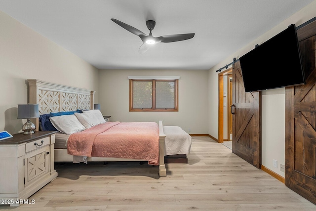 bedroom featuring a ceiling fan, light wood-style flooring, baseboards, and a barn door