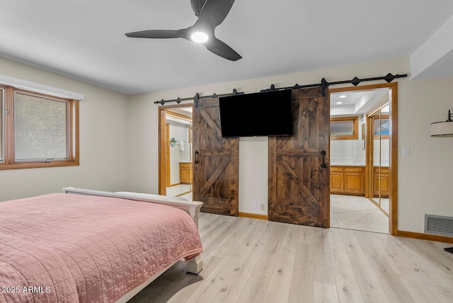 bedroom with a barn door, baseboards, visible vents, connected bathroom, and light wood-style flooring