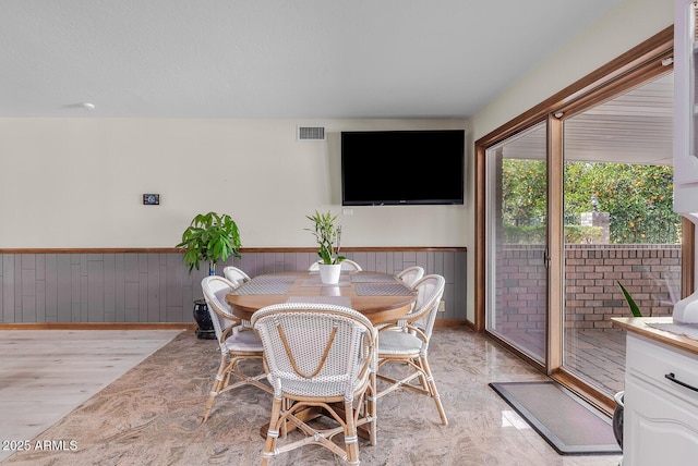 dining area featuring light wood-style flooring, wainscoting, and visible vents