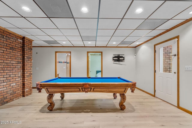 game room featuring a paneled ceiling, brick wall, baseboards, and light wood-style flooring