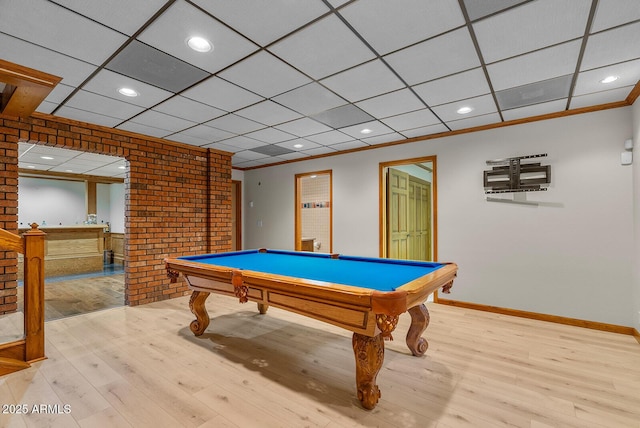 recreation room featuring a drop ceiling, light wood-style flooring, brick wall, baseboards, and ornamental molding