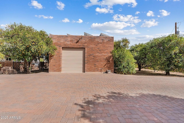 view of side of home with a garage, decorative driveway, brick siding, and fence