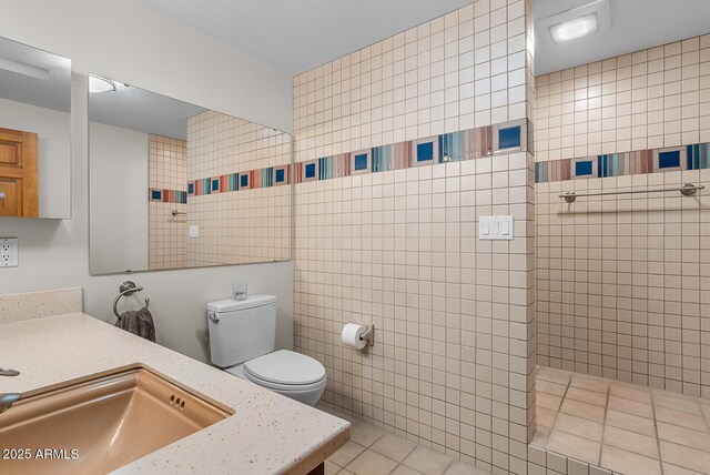 bathroom with a walk in shower, toilet, vanity, tile walls, and tile patterned floors