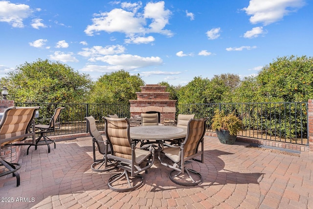 view of patio with an outdoor stone fireplace, fence, and outdoor dining area