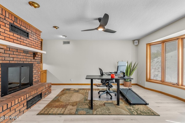 office space featuring baseboards, visible vents, wood finished floors, a textured ceiling, and a brick fireplace