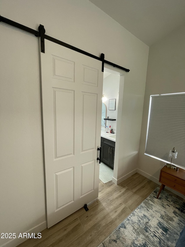 unfurnished bedroom featuring a barn door, ensuite bathroom, and light hardwood / wood-style floors