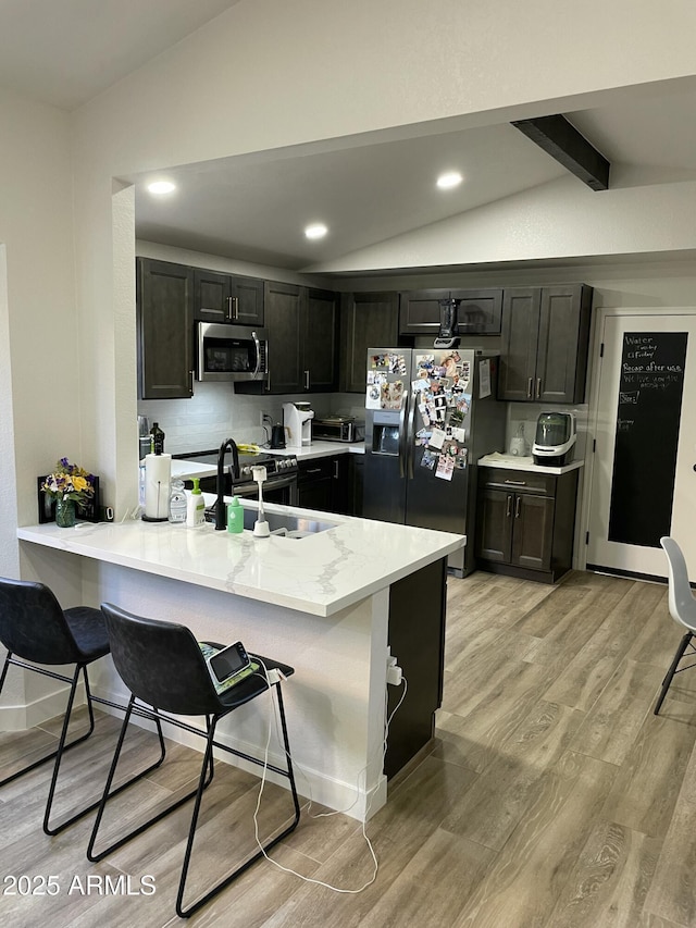 kitchen with vaulted ceiling with beams, a kitchen breakfast bar, kitchen peninsula, and stainless steel appliances