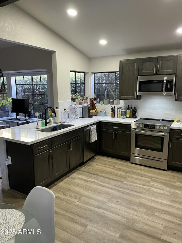 kitchen with sink, kitchen peninsula, vaulted ceiling, appliances with stainless steel finishes, and light wood-type flooring