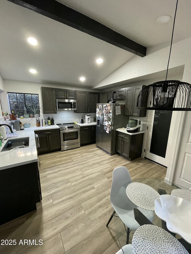 kitchen with appliances with stainless steel finishes, sink, decorative light fixtures, vaulted ceiling with beams, and light hardwood / wood-style floors