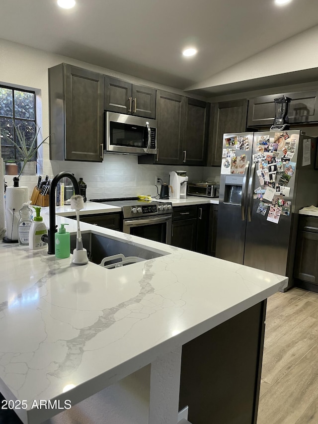 kitchen featuring lofted ceiling, decorative backsplash, light stone countertops, appliances with stainless steel finishes, and light hardwood / wood-style floors