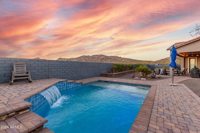 pool at dusk with a patio area and pool water feature