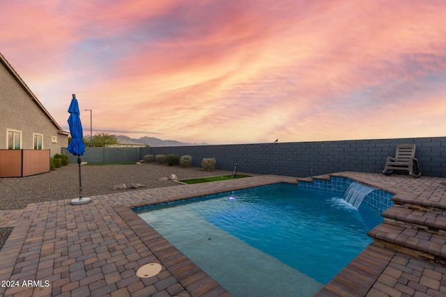 pool at dusk featuring pool water feature and a patio