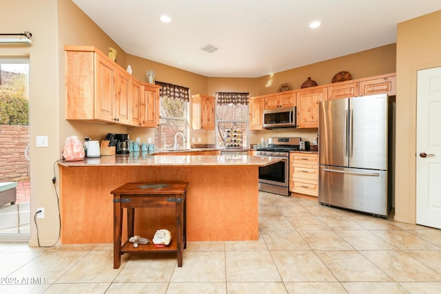 kitchen with light tile patterned floors, a breakfast bar, stainless steel appliances, light brown cabinetry, and kitchen peninsula