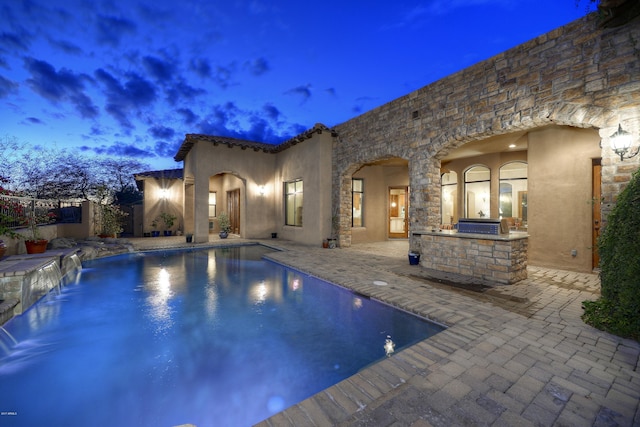 pool at dusk with a patio, pool water feature, and area for grilling