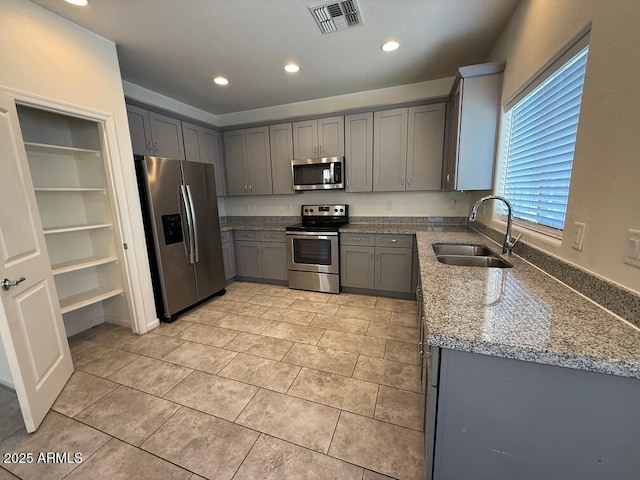 kitchen with light tile patterned flooring, stone countertops, sink, gray cabinetry, and stainless steel appliances