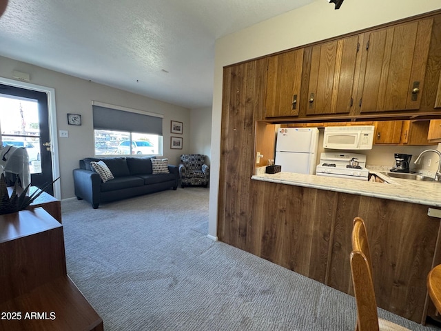 kitchen with white appliances, sink, light carpet, and a textured ceiling