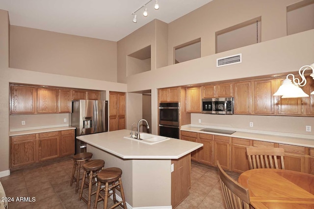 kitchen featuring sink, hanging light fixtures, a towering ceiling, a kitchen island with sink, and appliances with stainless steel finishes