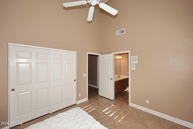 unfurnished bedroom featuring ceiling fan, tile patterned flooring, ensuite bathroom, a towering ceiling, and a closet