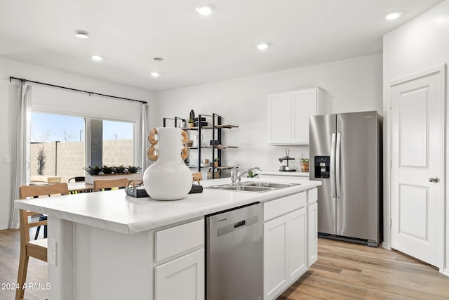 kitchen with an island with sink, appliances with stainless steel finishes, light wood-style floors, white cabinets, and a sink