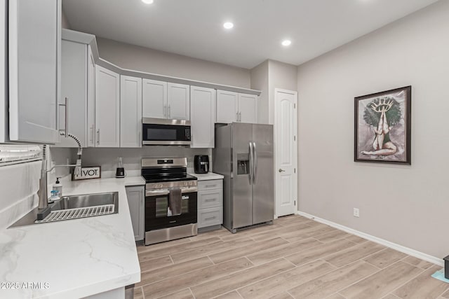 kitchen featuring light wood finished floors, a sink, baseboards, recessed lighting, and appliances with stainless steel finishes