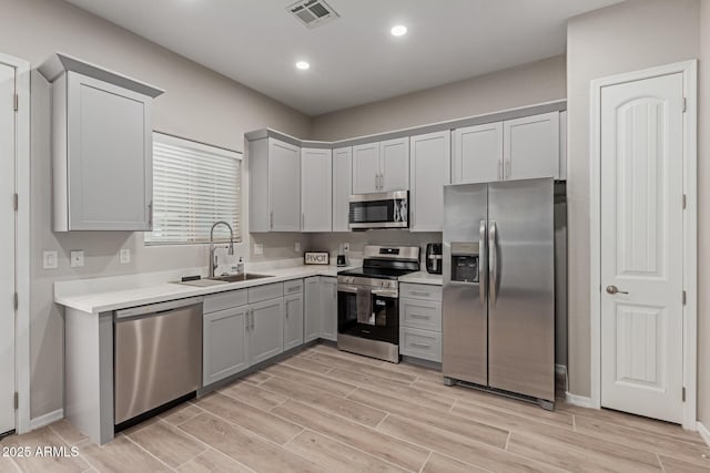kitchen with a sink, stainless steel appliances, wood finish floors, gray cabinetry, and visible vents