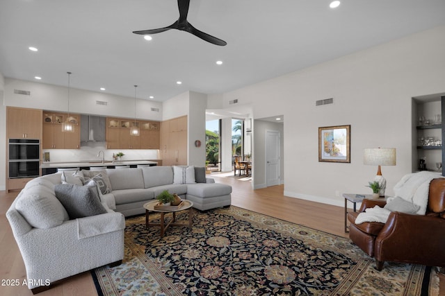 living room with sink, a towering ceiling, light hardwood / wood-style floors, and ceiling fan