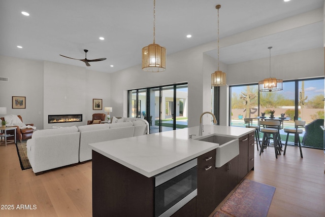 kitchen featuring stainless steel microwave, sink, decorative light fixtures, and a kitchen island with sink