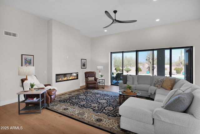 living room with ceiling fan, wood-type flooring, a fireplace, and a towering ceiling