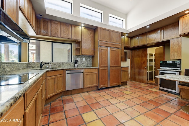 kitchen featuring a sink, backsplash, under cabinet range hood, and a healthy amount of sunlight