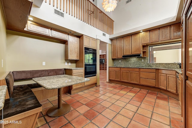 kitchen featuring visible vents, light tile patterned floors, decorative backsplash, a towering ceiling, and dobule oven black