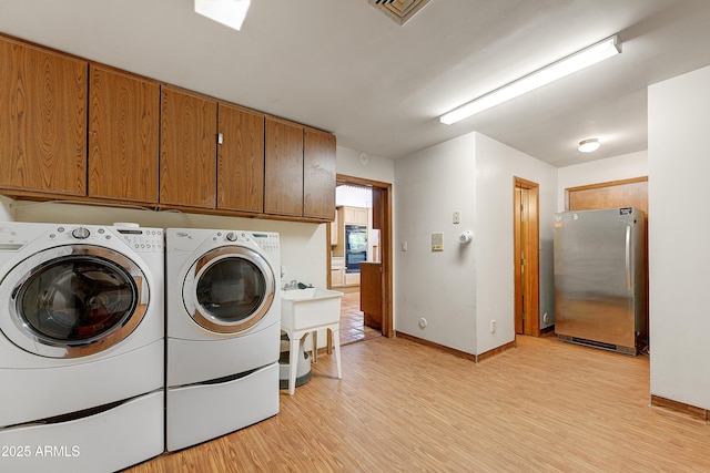 washroom with baseboards, visible vents, washing machine and clothes dryer, cabinet space, and light wood-style floors