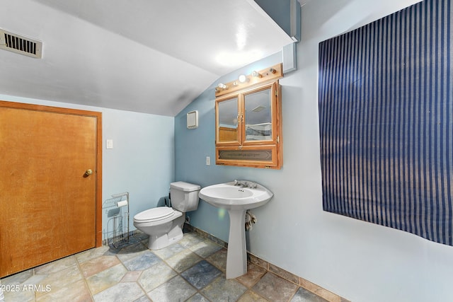 half bath featuring baseboards, visible vents, lofted ceiling, stone finish floor, and toilet