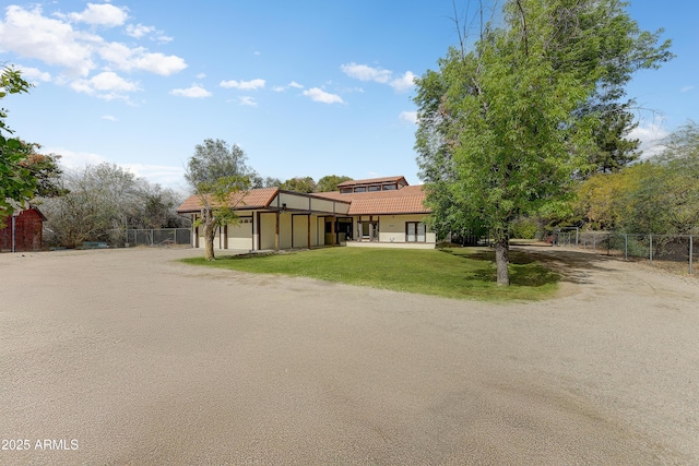 view of front of home with a front yard, fence, stucco siding, dirt driveway, and a tile roof