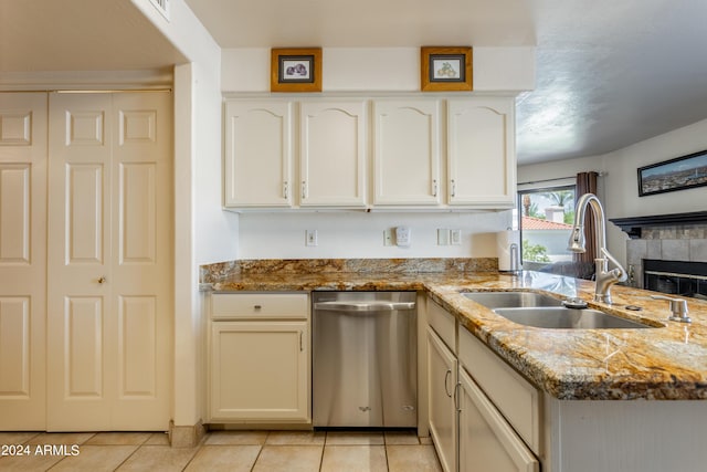 kitchen with light tile patterned flooring, stone counters, stainless steel dishwasher, a tile fireplace, and sink