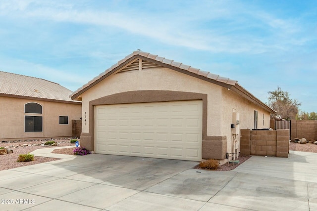 view of front of home featuring an attached garage, fence, concrete driveway, a tiled roof, and stucco siding